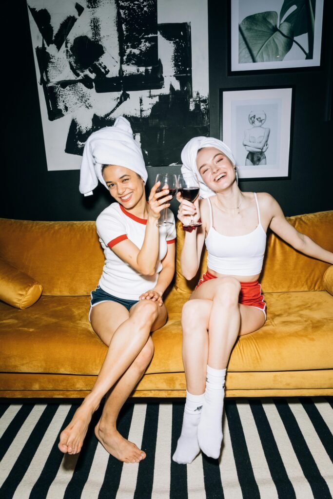 Two happy young women enjoying wine together on a cozy sofa at home.